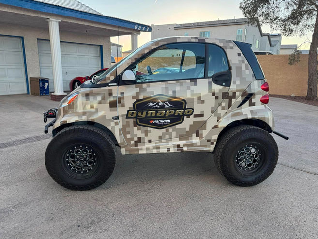 Lifted Smart car with Dynapro logo and large tires, LIFTED SMART FORTWO in yard.