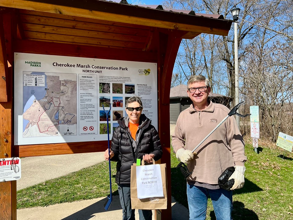 A man and woman pose with clean-up equipment before picking up trash for Earth Day. They stand in front of an information kiosk for the Cherokee Marsh North Unit.