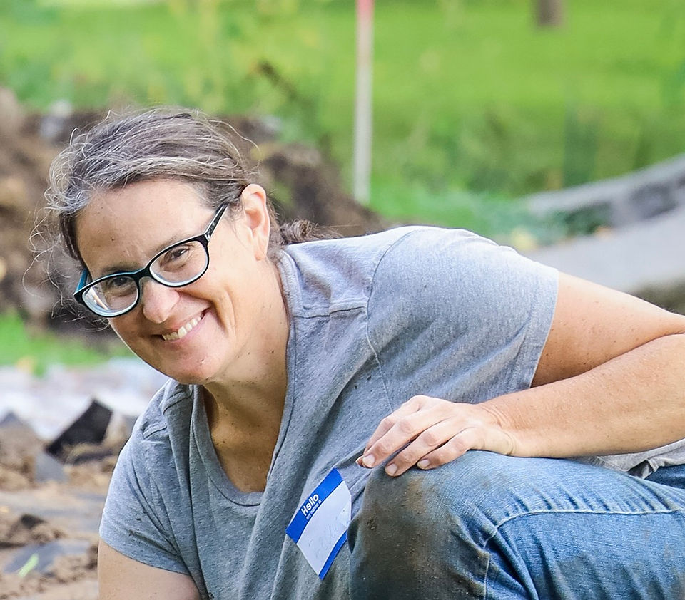  Becca Dymzarov, wearing a gray t-shirt and jeans, smiles at the camera as she works on planting plugs of native plants