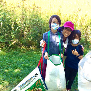 A mom and two kids hold seed-collecting bags at the edge of a prairie in autumn