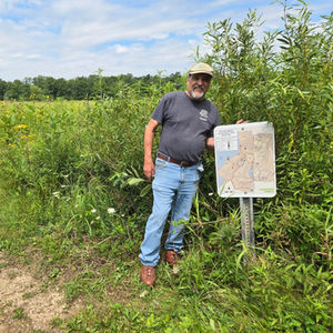Volunteer Jim Mand stands on a trail through a prairie at Cherokee Marsh next to a new trail map on a post.