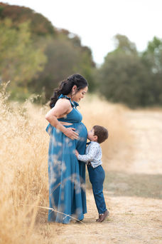 A beautiful maternity photography session taken by the best Sacramento maternity photographer, featuring a glowing mother-to-be in stunning settings. The images showcase a mix of posed and candid moments with her family, including her partner and children, set against rustic barns, lush greenery, and serene sunset backdrops. The session highlights elegant maternity gowns in shades of blue and pink, capturing the joy, love, and anticipation of this special time.
