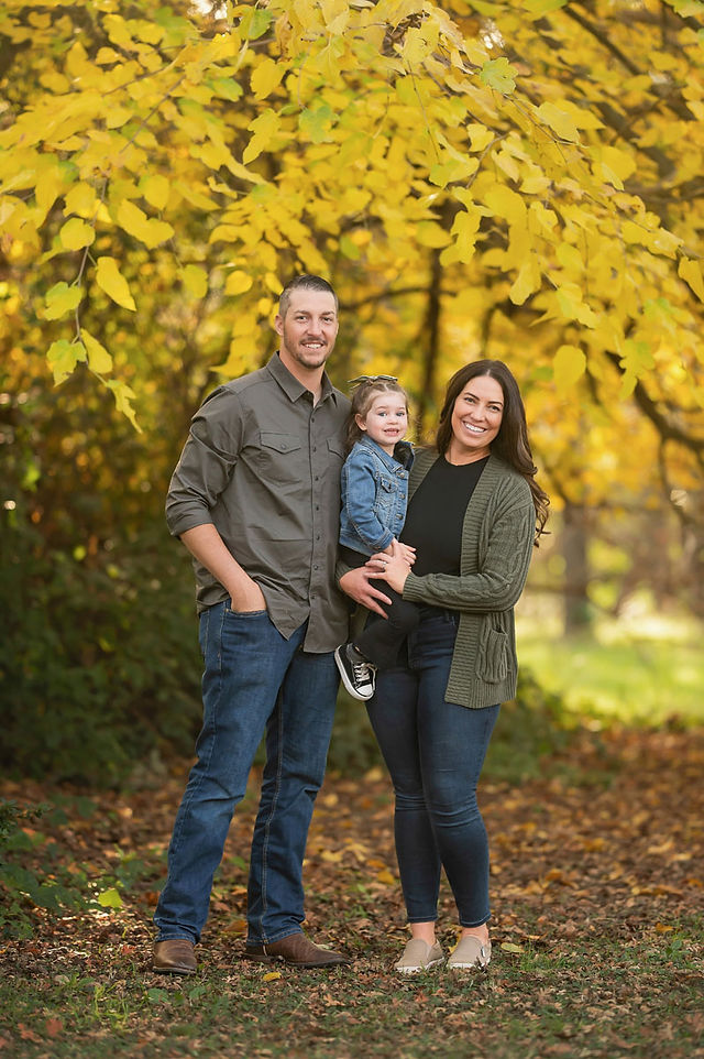Family with a young child during a fall family photography session surrounded by golden trees at the Iris Farm in Loomis, California.