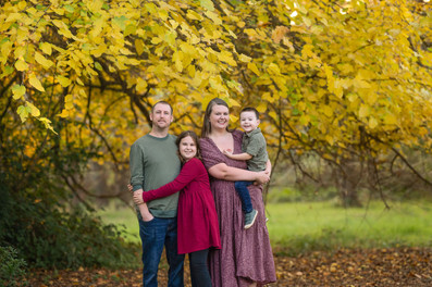 Family of four posing together during a fall family photography session surrounded by golden trees at the Iris Farm in Loomis, California.