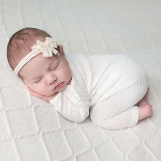 Newborn baby girl wrapped in white swaddle with a flower headband, sleeping peacefully on a white knit blanket. Taken by Sacramento maternity and newborn photographer Kristina Martin