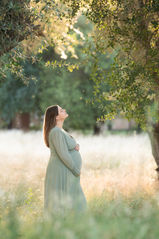 Pregnant woman in a flowing green dress standing in a golden meadow, bathed in soft, natural light taken by Sacramento photographer Kristina Martin Photography.