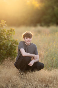 Izzack poses in an open field during sunset, capturing the golden light as it shines through the grass. Shot by the best Sacramento senior photographer.