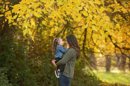 Family with a young child during a fall family photography session surrounded by golden trees at the Iris Farm in Loomis, California.