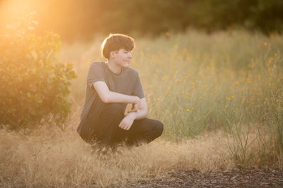 Izzack poses in an open field during sunset, capturing the golden light as it shines through the grass. Shot by the best Sacramento senior photographer.