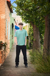 Izzack stands among vibrant, colorful cottages near Capitola Beach, showcasing the charm of the seaside town. Shot by the best Sacramento senior photographer.