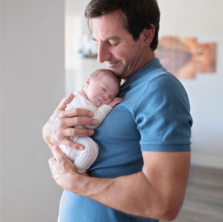 Father holding newborn baby girl close, smiling warmly at her. Taken by Sacramento maternity and newborn photographer Kristina Martin
