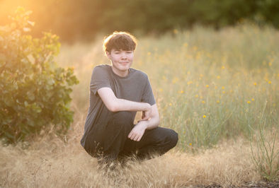 Izzack poses in an open field during sunset, capturing the golden light as it shines through the grass. Shot by the best Sacramento senior photographer.