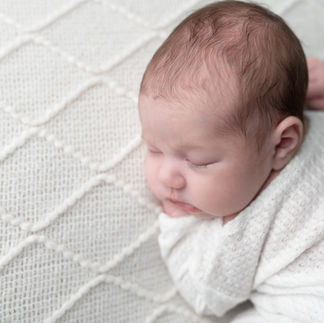 Profile view of a newborn baby girl sleeping, wrapped in a white swaddle on a white knit blanket. Taken by Sacramento maternity and newborn photographer Kristina Martin