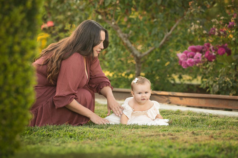 One year milestone session in Rocklin featuring a baby girl in a mauve velvet dress with her family. Photos captured in a rose garden, orchard, and near a quaint little church by Sacramento family photographer Kristina Martin.