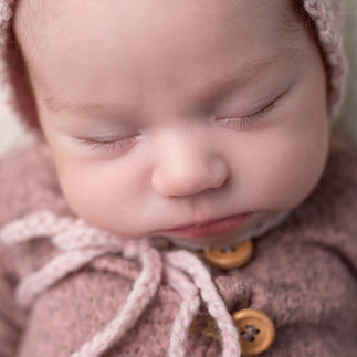 Close-up macro of newborn baby girl's face wrapped in a light pink knitted outfit and bonnet, sleeping peacefully with eyes closed. Taken by Sacramento maternity and newborn photographer Kristina Martin