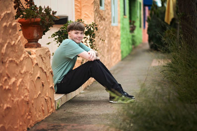 Izzack stands among vibrant, colorful cottages near Capitola Beach, showcasing the charm of the seaside town. Shot by the best Sacramento senior photographer.