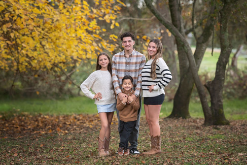 Large extended family posing together among golden fall trees during a family photography session at the Iris Farm in Loomis, California.