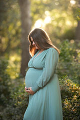 Side profile of a pregnant woman in a green dress, looking down at her belly while standing in a wooded area taken by Sacramento photographer Kristina Martin Photography.