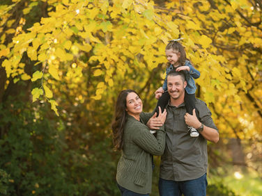 Family with a young child during a fall family photography session surrounded by golden trees at the Iris Farm in Loomis, California.
