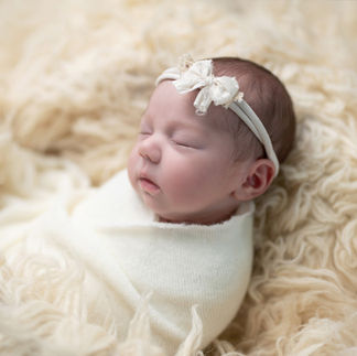 Side profile of a newborn baby girl wrapped in a white swaddle, sleeping on a cream-colored furry blanket. Taken by Sacramento maternity and newborn photographer Kristina Martin