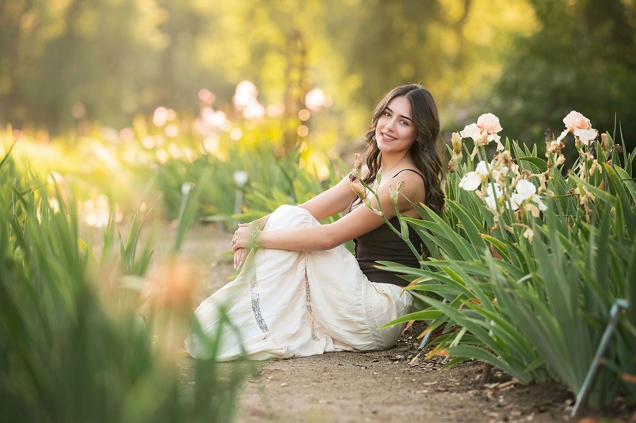 Sacramento senior photographer capturing a golden hour iris farm senior session with blooming flowers, artistic natural light, cap and gown portraits, and personality-filled senior photography.
