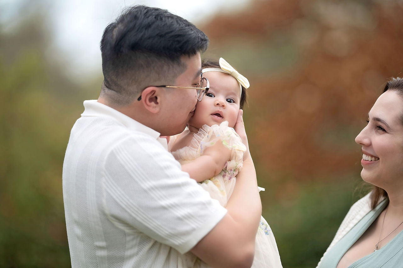 Family session at a blooming botanical garden in Sacramento featuring parents with their three month old baby girl, soft floral backdrops, candid moments, and natural light photography by a local Sacramento baby and family photographer.