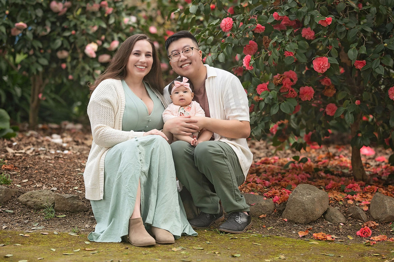 Family session at a blooming botanical garden in Sacramento featuring parents with their three month old baby girl, soft floral backdrops, candid moments, and natural light photography by a local Sacramento baby and family photographer.
