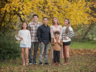 Large extended family posing together among golden fall trees during a family photography session at the Iris Farm in Loomis, California.