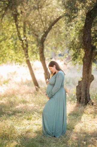 Pregnant woman standing alone in a sunlit meadow, surrounded by trees taken by Sacramento photographer Kristina Martin Photography.