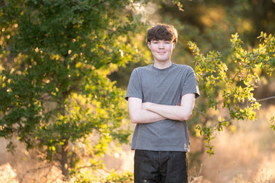 Izzack poses in an open field during sunset, capturing the golden light as it shines through the grass. Shot by the best Sacramento senior photographer.
