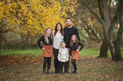 Large extended family posing together among golden fall trees during a family photography session at the Iris Farm in Loomis, California.