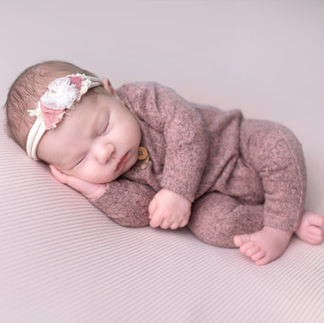 Newborn baby girl sleeping in a light pink knitted outfit, with hands tucked under her chin. Taken by Sacramento maternity and newborn photographer Kristina Martin