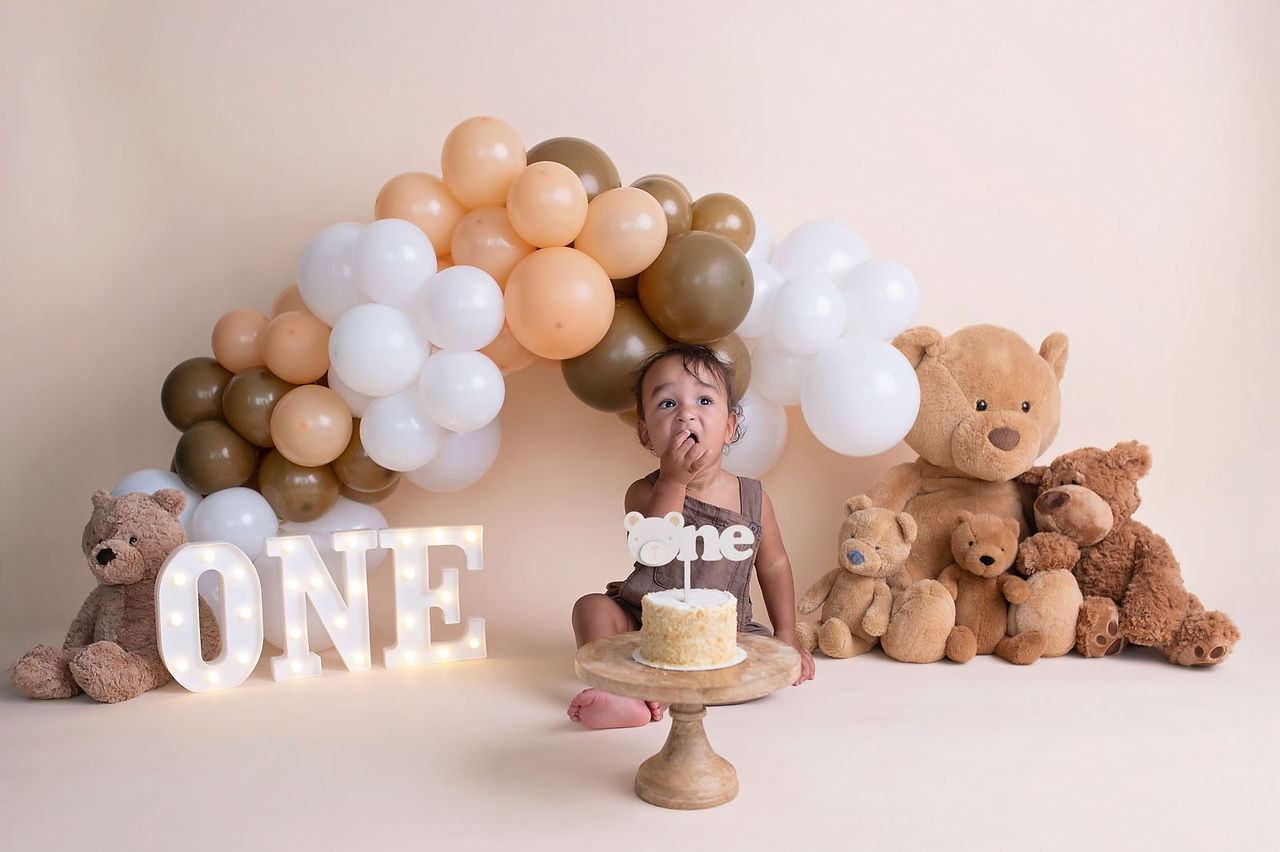 Cake smash session by the best Sacramento photographer featuring a teddy bear theme, neutral balloon arch, and first birthday setup in a studio setting.