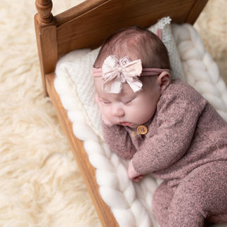 Newborn baby girl wrapped in a light pink knitted outfit, sleeping on a tiny wooden bed with white bedding. Taken by Sacramento maternity and newborn photographer Kristina Martin