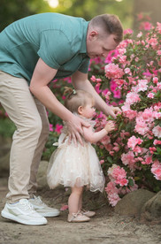 Maternity and family portraits at a botanical garden in Carmichael with spring flowers in bloom, featuring a mother in pink and pearl dresses, her partner, and their one year old daughter in soft natural light.