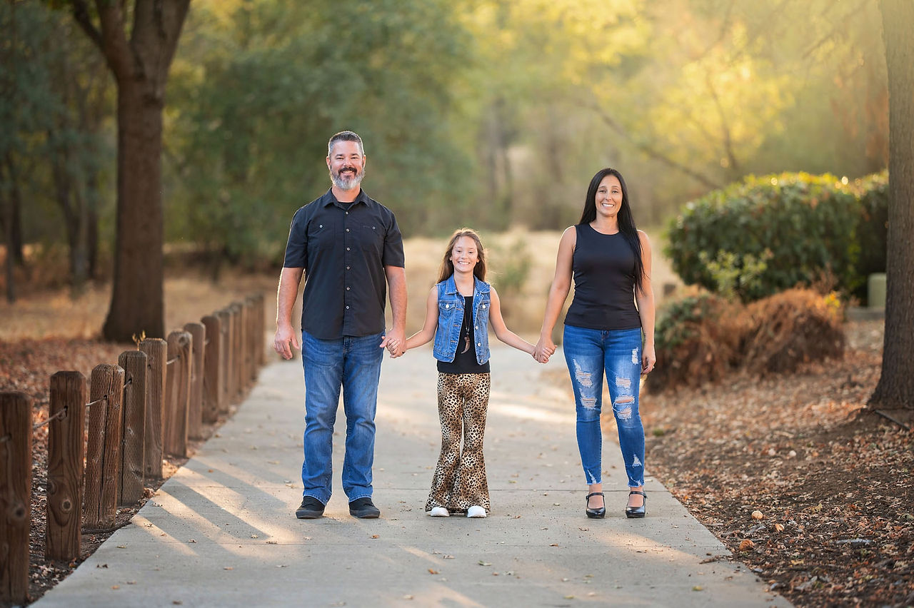 Family photography session at the Citrus Heights Nature Preserve featuring a family walking along a wooden bridge surrounded by trees and warm evening light.