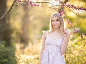 High school senior girl posing in a blooming botanical garden in Sacramento during spring, wearing multiple outfits including a navy dress, a soft pink dress, and college gear, captured in golden hour light by a Sacramento senior photographer.