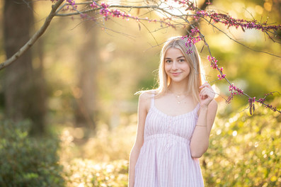 High school senior girl posing in a blooming botanical garden in Sacramento during spring, wearing multiple outfits including a navy dress, a soft pink dress, and college gear, captured in golden hour light by a Sacramento senior photographer.