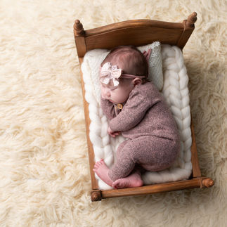Newborn baby girl wrapped in a light pink knitted outfit, sleeping on a tiny wooden bed with white bedding. Taken by Sacramento maternity and newborn photographer Kristina Martin