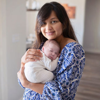 Mother smiling as she holds her newborn baby girl wrapped in a white swaddle. Taken by Sacramento maternity and newborn photographer Kristina Martin