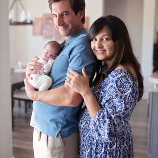 Happy parents standing in their living room, each holding their newborn baby girl close and smiling. Taken by Sacramento maternity and newborn photographer Kristina Martin
