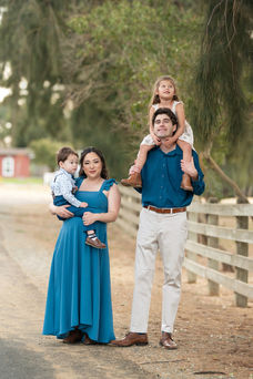 A beautiful maternity photography session taken by the best Sacramento maternity photographer, featuring a glowing mother-to-be in stunning settings. The images showcase a mix of posed and candid moments with her family, including her partner and children, set against rustic barns, lush greenery, and serene sunset backdrops. The session highlights elegant maternity gowns in shades of blue and pink, capturing the joy, love, and anticipation of this special time.