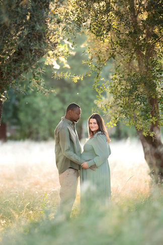 Close-up of a couple standing in a sunlit forest, with the husband placing his hand on the pregnant wife’s belly taken by Sacramento photographer Kristina Martin Photography.
