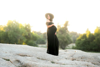 Sasha in a black maternity dress, holding her belly while standing in the lake, captured by the best Sacramento maternity photographer Kristina Martin