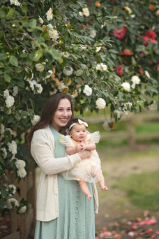 Family session at a blooming botanical garden in Sacramento featuring parents with their three month old baby girl, soft floral backdrops, candid moments, and natural light photography by a local Sacramento baby and family photographer.