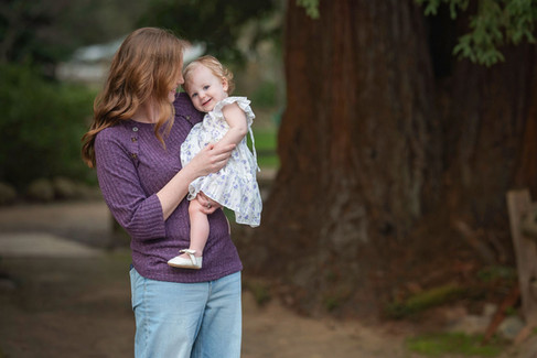 Sacramento baby photographer capturing a one year milestone session at a botanical garden with blooming flowers, toddler girls in soft dresses, candid sibling moments, and natural family portraits in a lush outdoor setting.