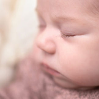 Close-up macro of a newborn baby girl's face, wrapped in a light pink knitted outfit, with eyes closed in sleep. Focus falls on the delicate eyelashes. Taken by Sacramento maternity and newborn photographer Kristina Martin