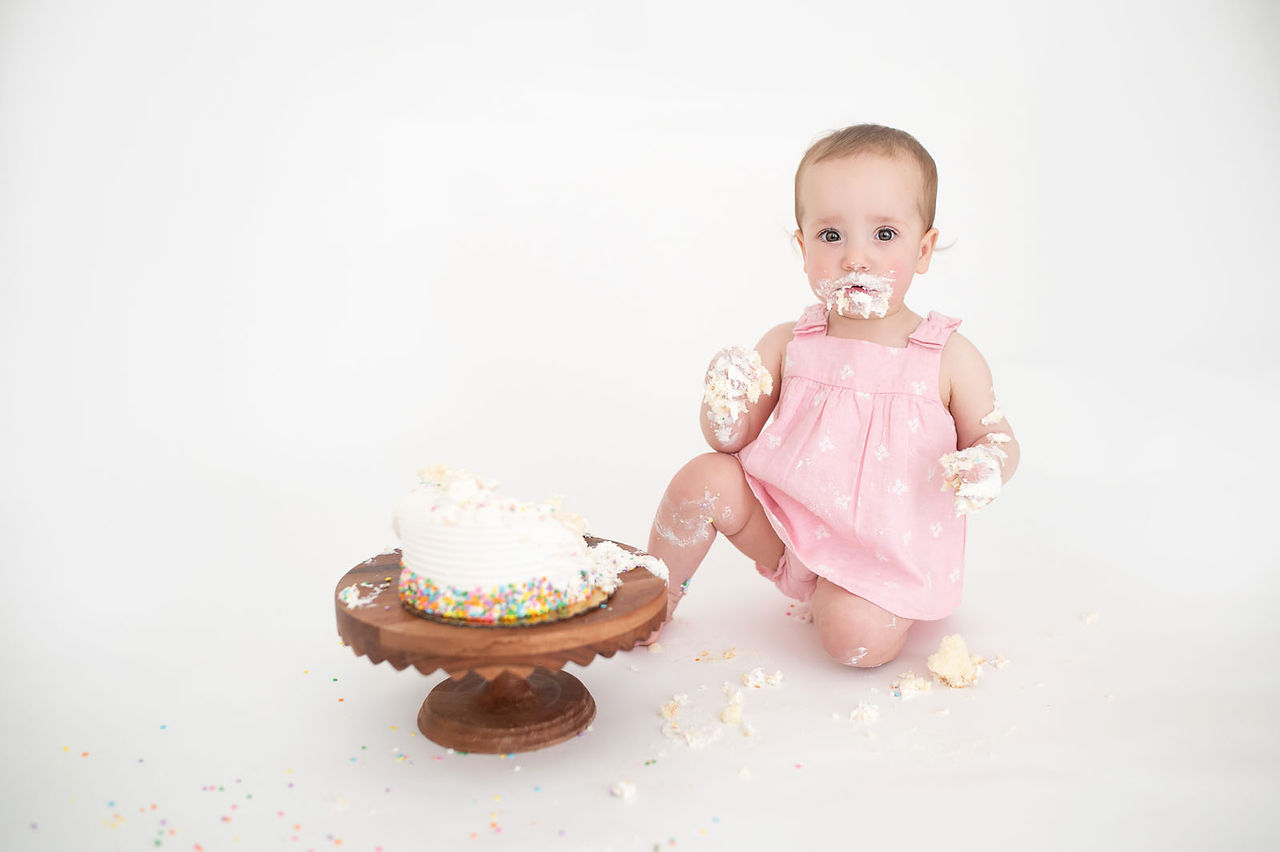 Roseville studio one year milestone session featuring a baby girl, simple white cake smash setup, natural sibling moments, and soft backlit family photography by a Sacramento photographer.