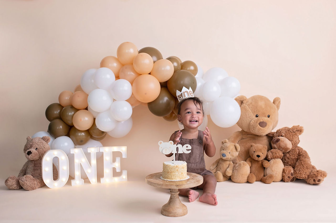 Cake smash session by the best Sacramento photographer featuring a teddy bear theme, neutral balloon arch, and first birthday setup in a studio setting.