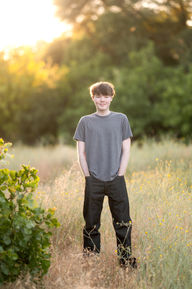 Izzack poses in an open field during sunset, capturing the golden light as it shines through the grass. Shot by the best Sacramento senior photographer.